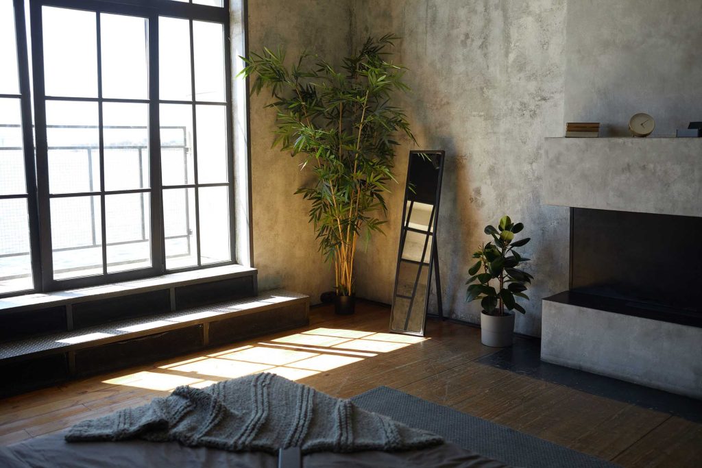 Salón de estilo industrial con gran ventana, plantas decorativas y chimenea moderna