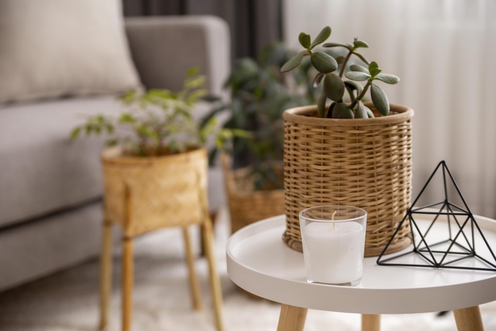Detalles decorativos con plantas en cestas de fibra, mesa auxiliar blanca y vela en un salón de estilo mediterráneo en Málaga